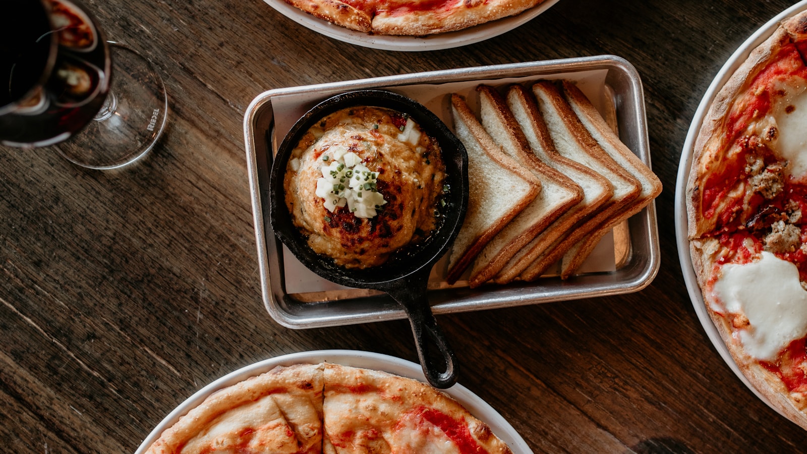 Pizza, Brot und ein Gericht in einer kleinen Pfanne auf einem Restauranttisch.